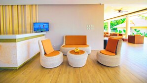 A reception area with a TV displaying a program, wicker chairs with orange cushions, and a wooden floor. - Bohol Shores (Dauis)