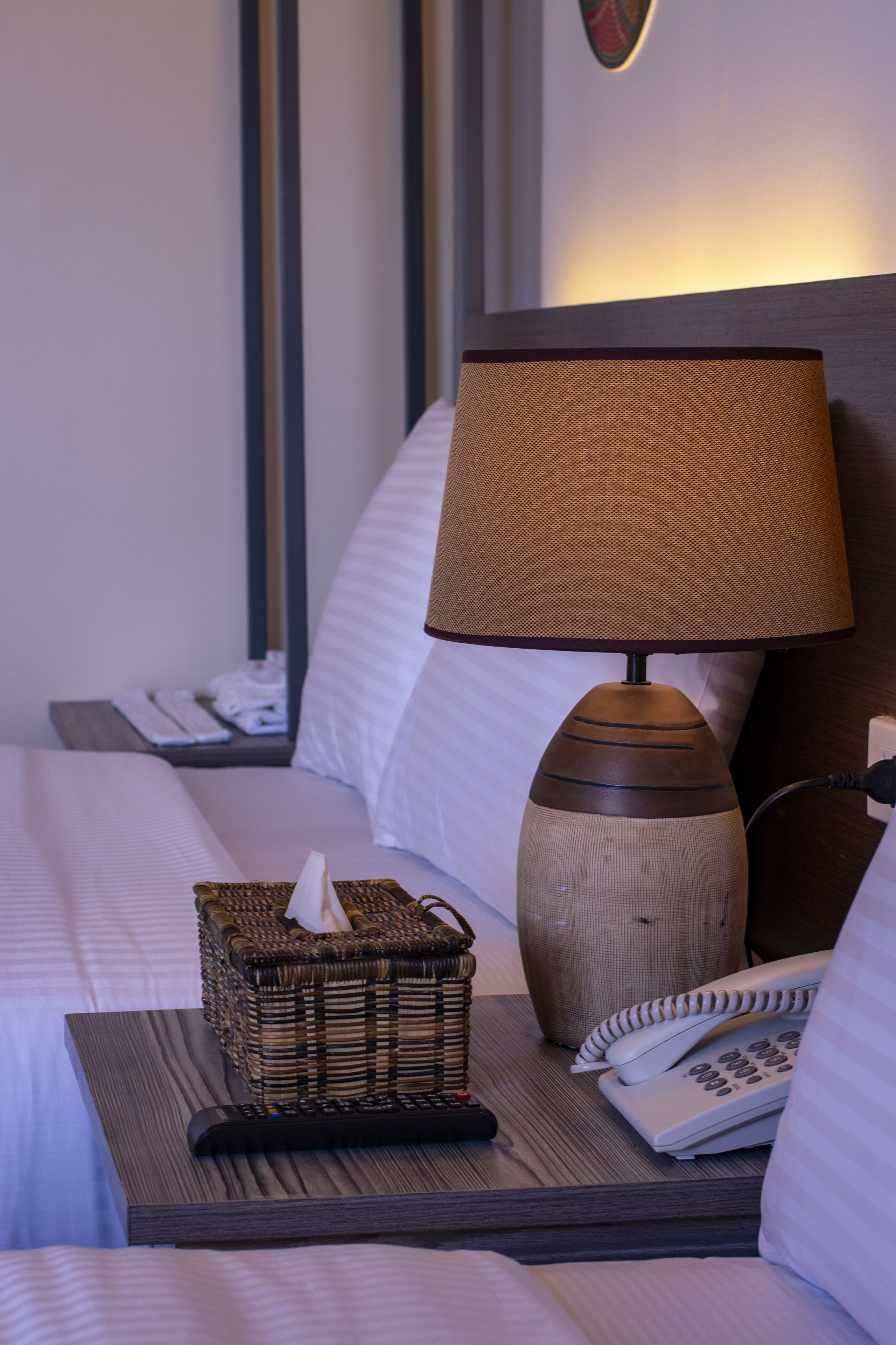 A neatly made bed with white linens, a bedside lamp, a tissue box, and a telephone on a wooden nightstand.