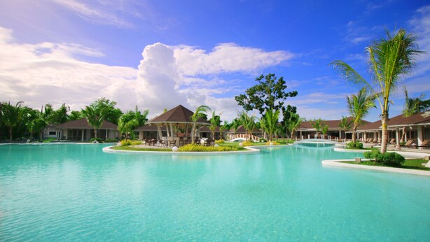 A resort with a large swimming pool, palm trees, and resort buildings. - Bohol Shores (Dauis)