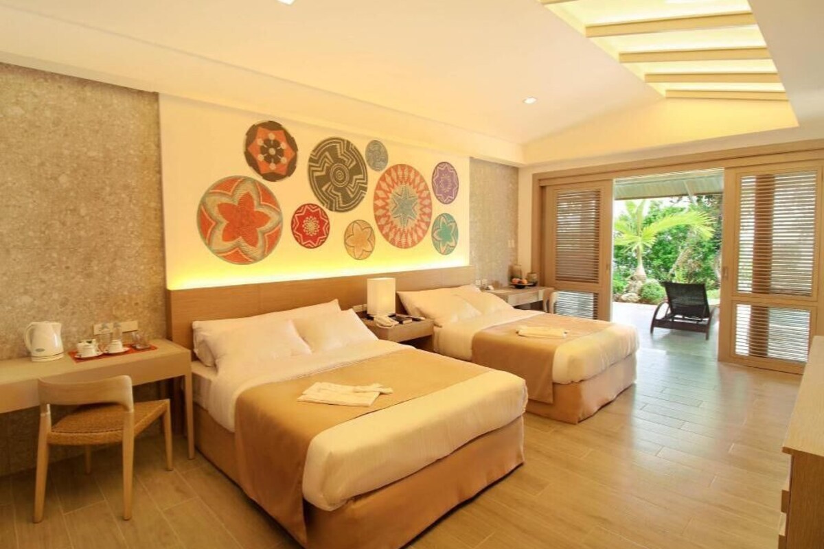 A hotel room with two beds, a desk, a chair, and a wall decorated with circular patterns.