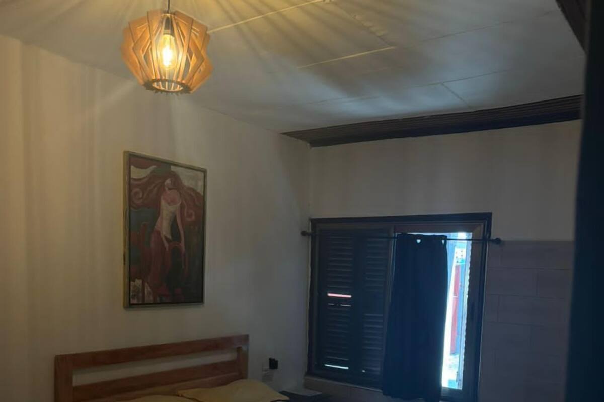 A bedroom with a wooden bed, a hanging light fixture, a window with shutters, and a painting on the wall.