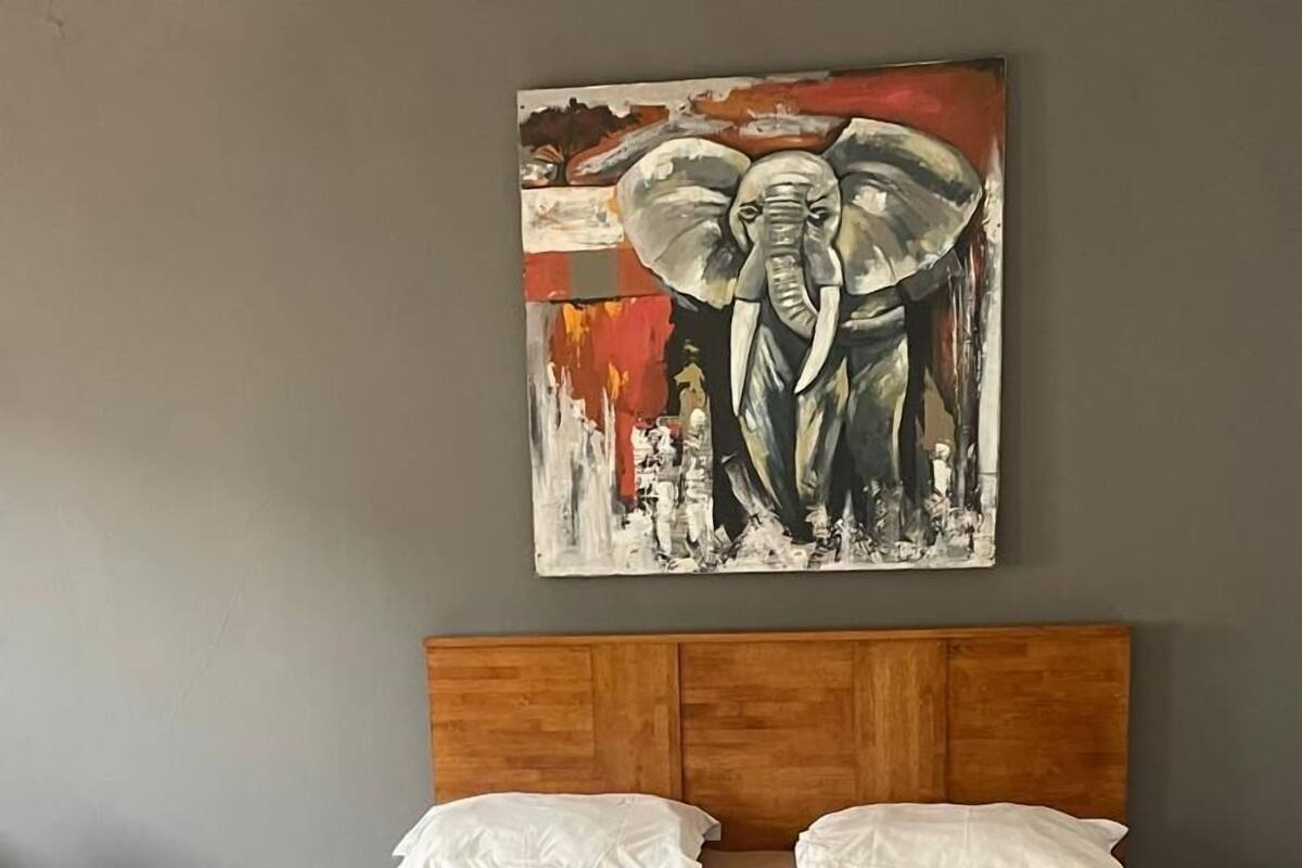 A bedroom with a wooden headboard, a blue bedspread, and a painting of an elephant on the wall.