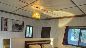 Ein Schlafzimmer mit einem hölzernen Bett, einer Deckenleuchte, einem Fenster mit Vorhängen und einem Sessel.