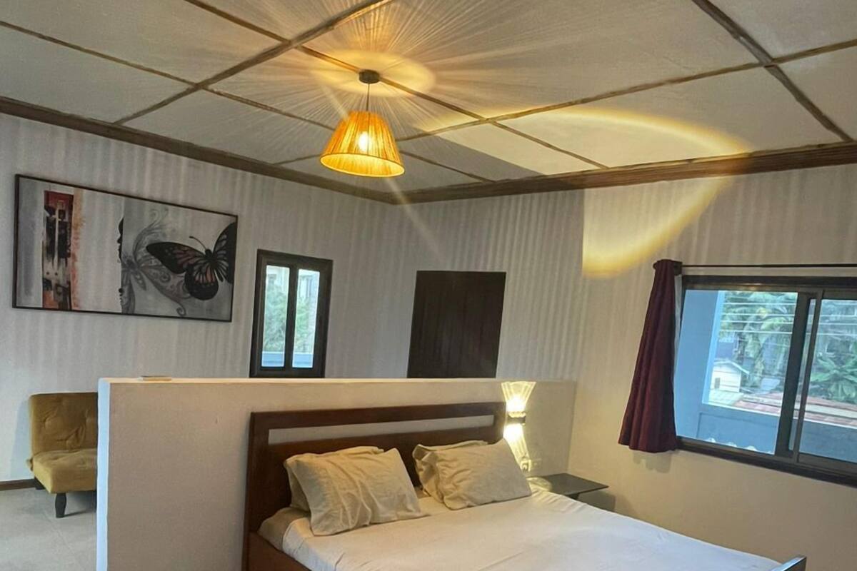 A bedroom with a wooden bed, a ceiling light, a window with curtains, and a chair.