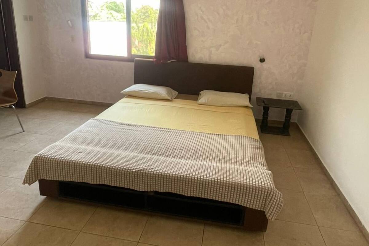 A bedroom with a bed, a window with curtains, an air conditioning unit, and a hanging light fixture.