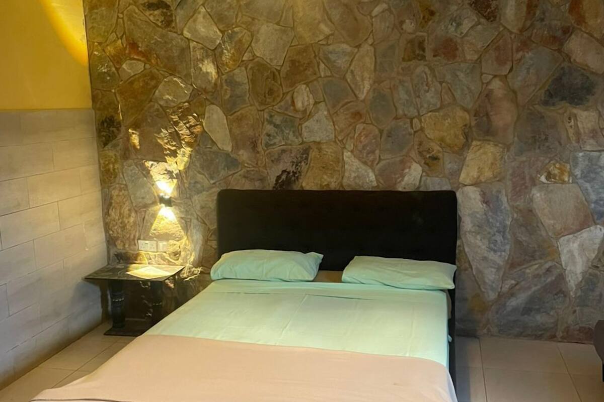 A bedroom with a stone wall, a bed with a black headboard, and a unique hanging light fixture.