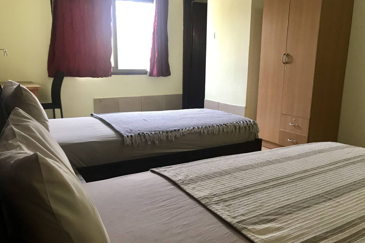 A room with two beds, a wardrobe, and a window with curtains.