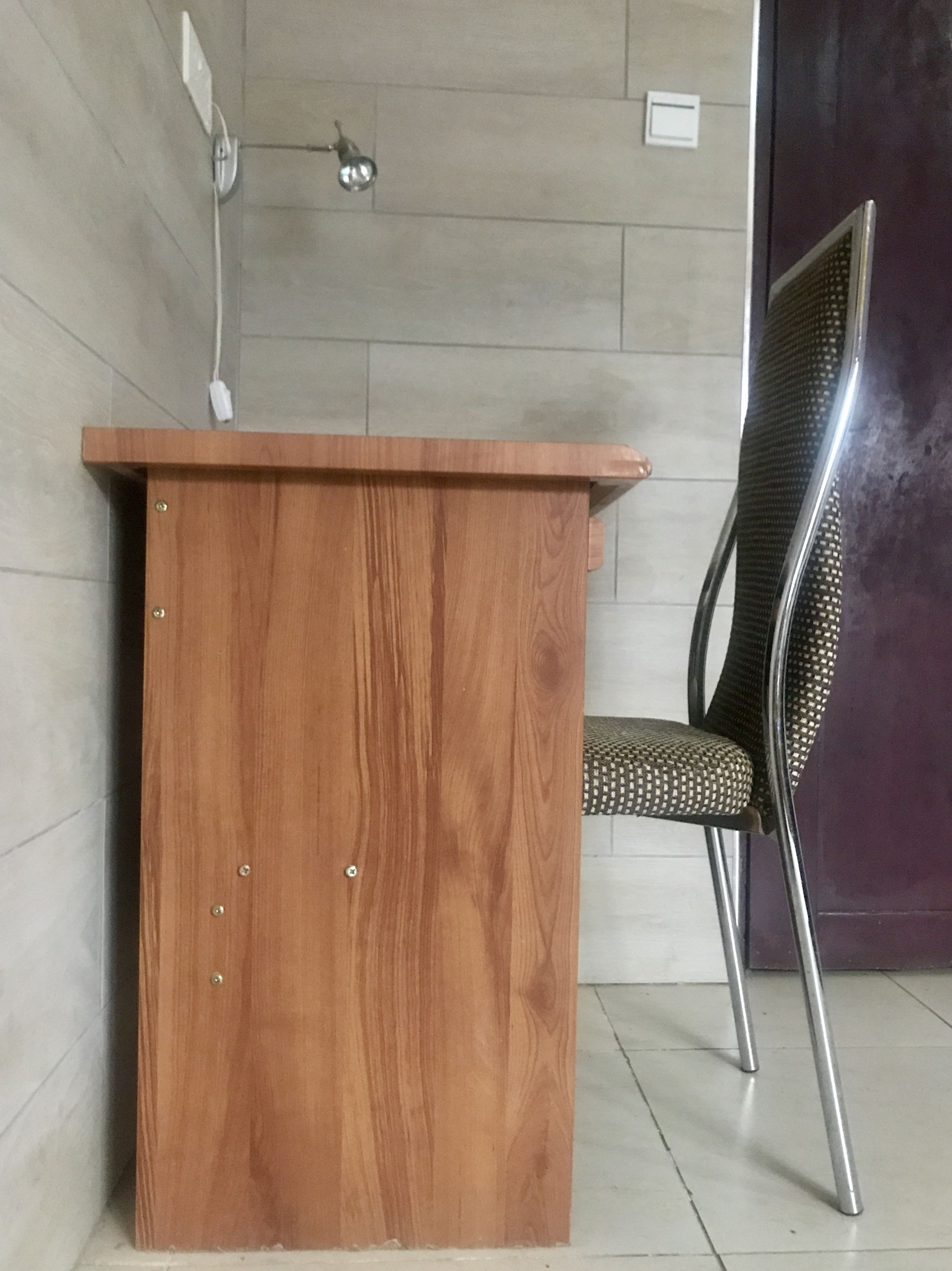 A wooden desk with a chair in a room with tiled walls and a door.