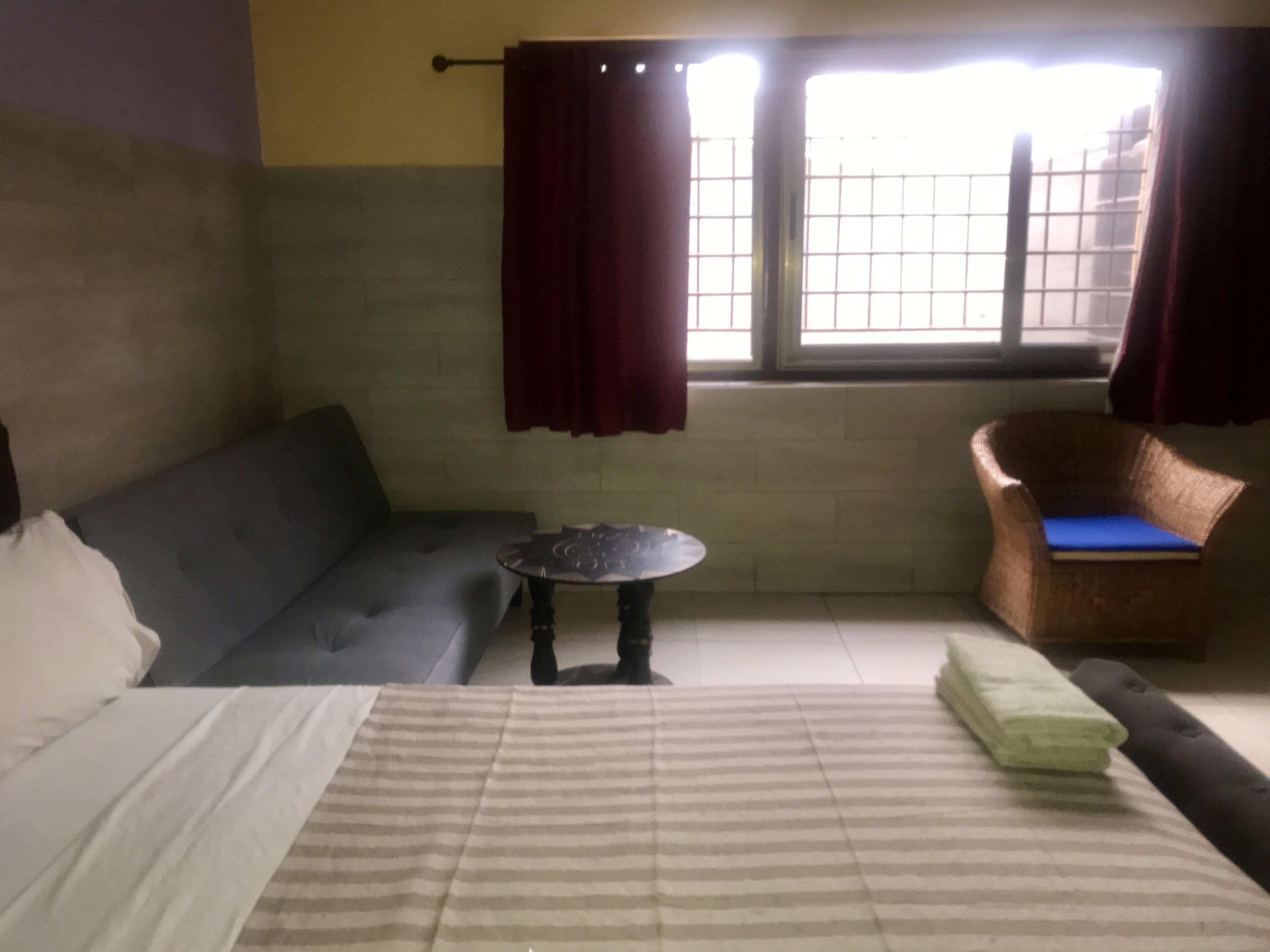 A room with a bed, a sofa, a small round table, a wicker chair, and a window with curtains.