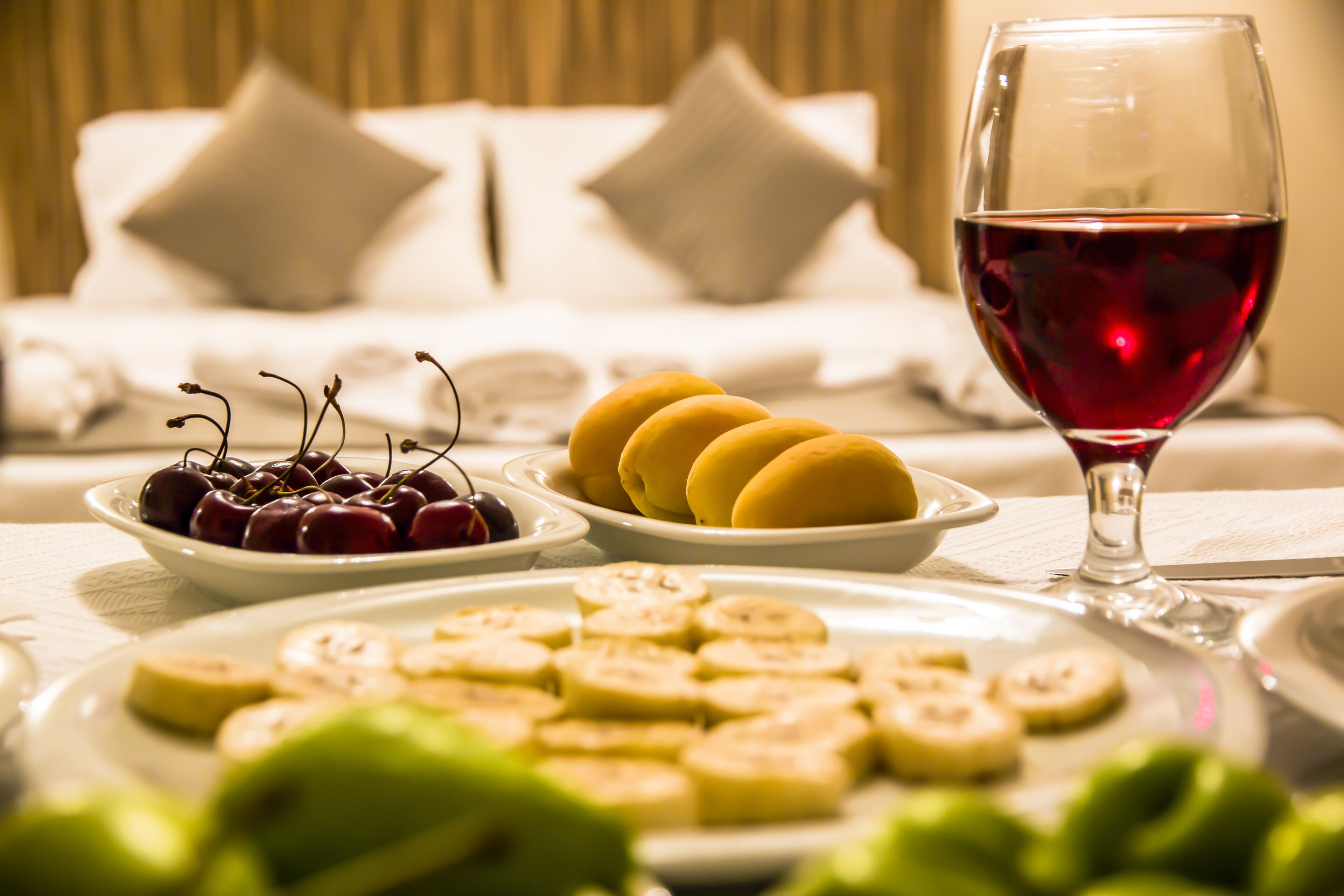 Une table à manger avec des assiettes de cerises, des bananes et un verre de vin rouge.