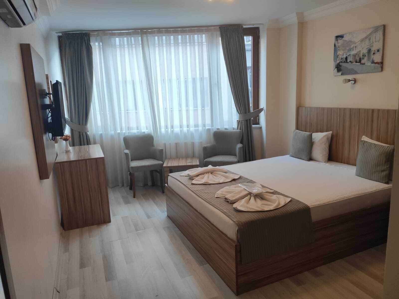 A hotel room with a large bed, a desk, two chairs, a TV, and a painting on the wall.