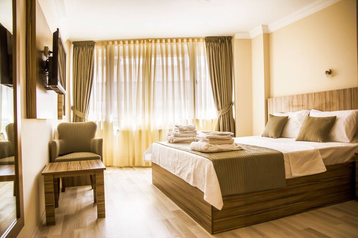 Una habitación de hotel con una cama, una silla, un televisor y un ventanal con cortinas.