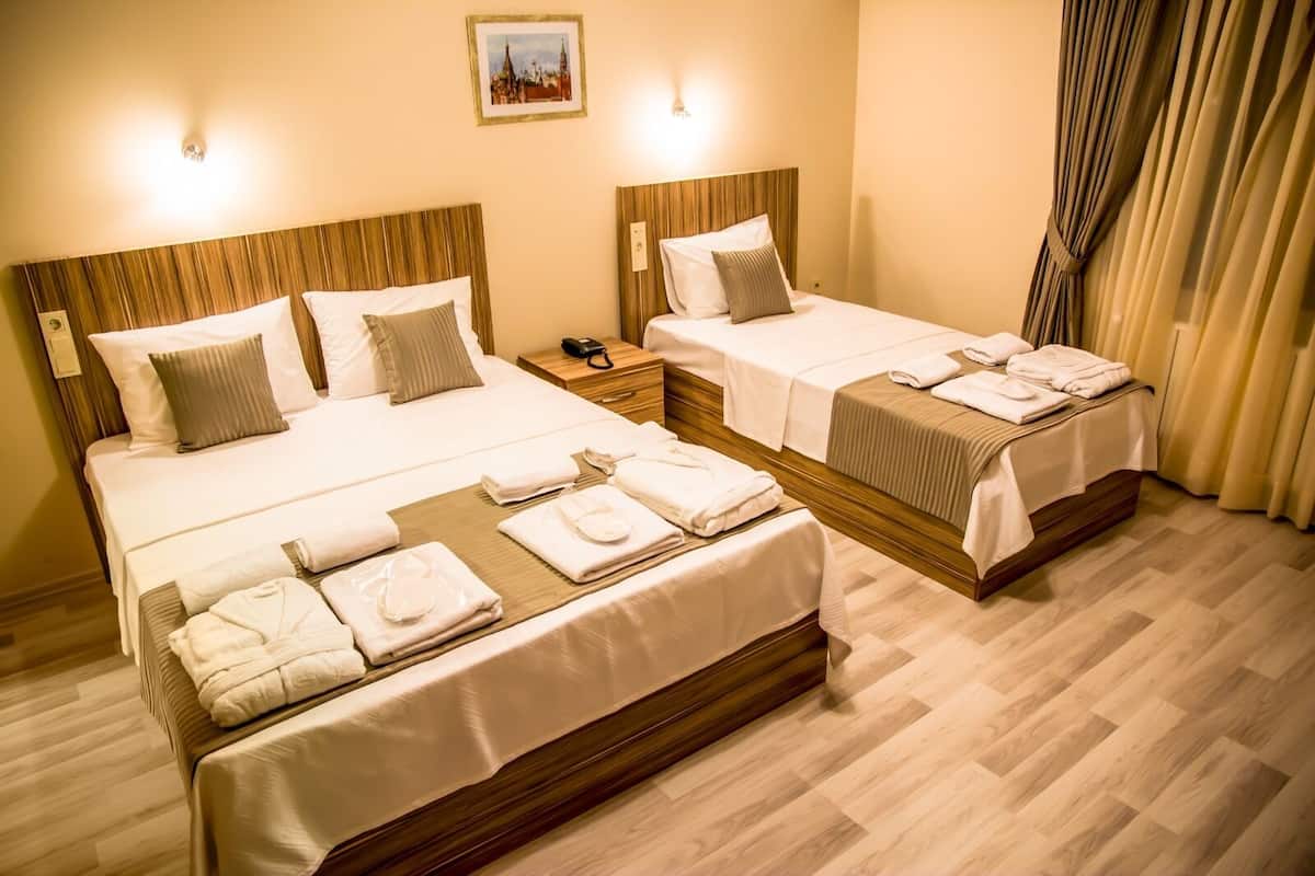 Habitación de hotel con dos camas, cada una con ropa de cama y almohadas blancas, cabeceros de madera, mesitas de noche con lámparas y un cuadro en la pared.
