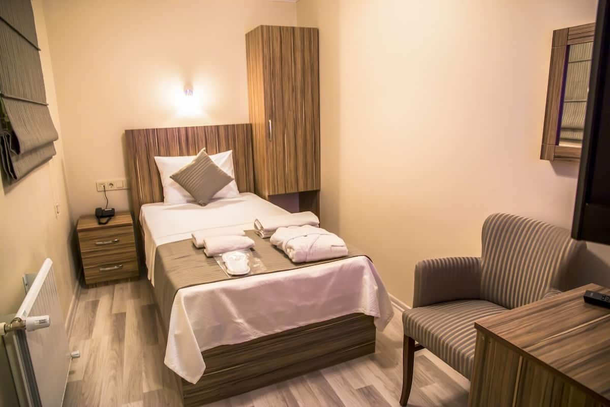 Una habitación de hotel con cama, mesita de noche, silla y armario de madera.