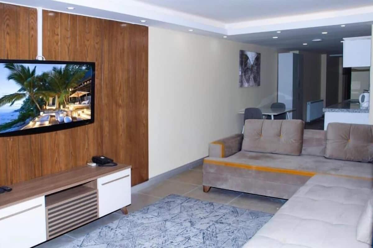 Una sala moderna con un televisor de pantalla plana, un sofá color beige y una pared decorativa de madera.