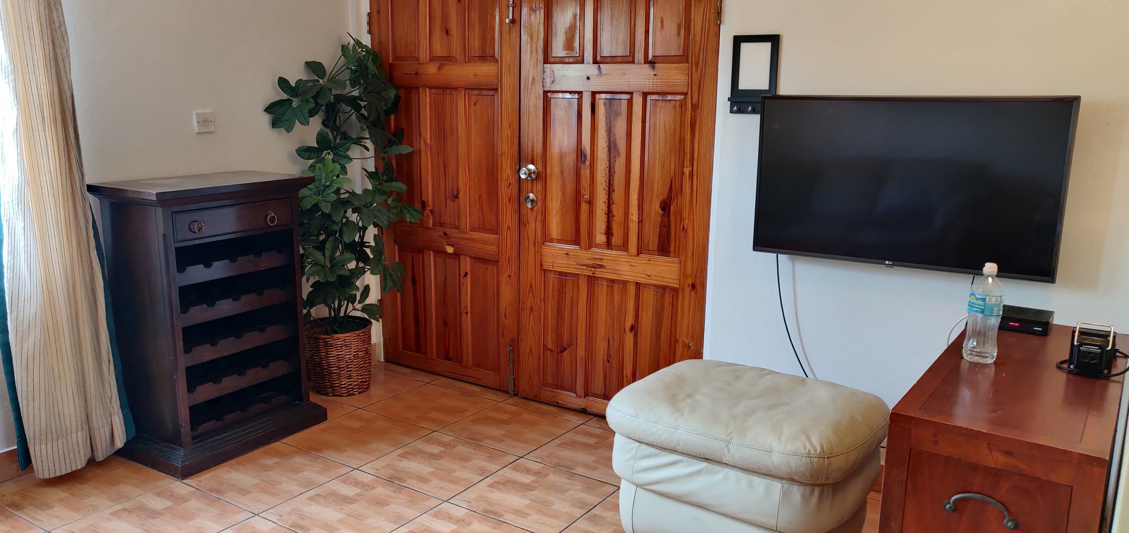 A room with a wooden wardrobe, a television mounted on the wall, a potted plant, and a cushioned bench.