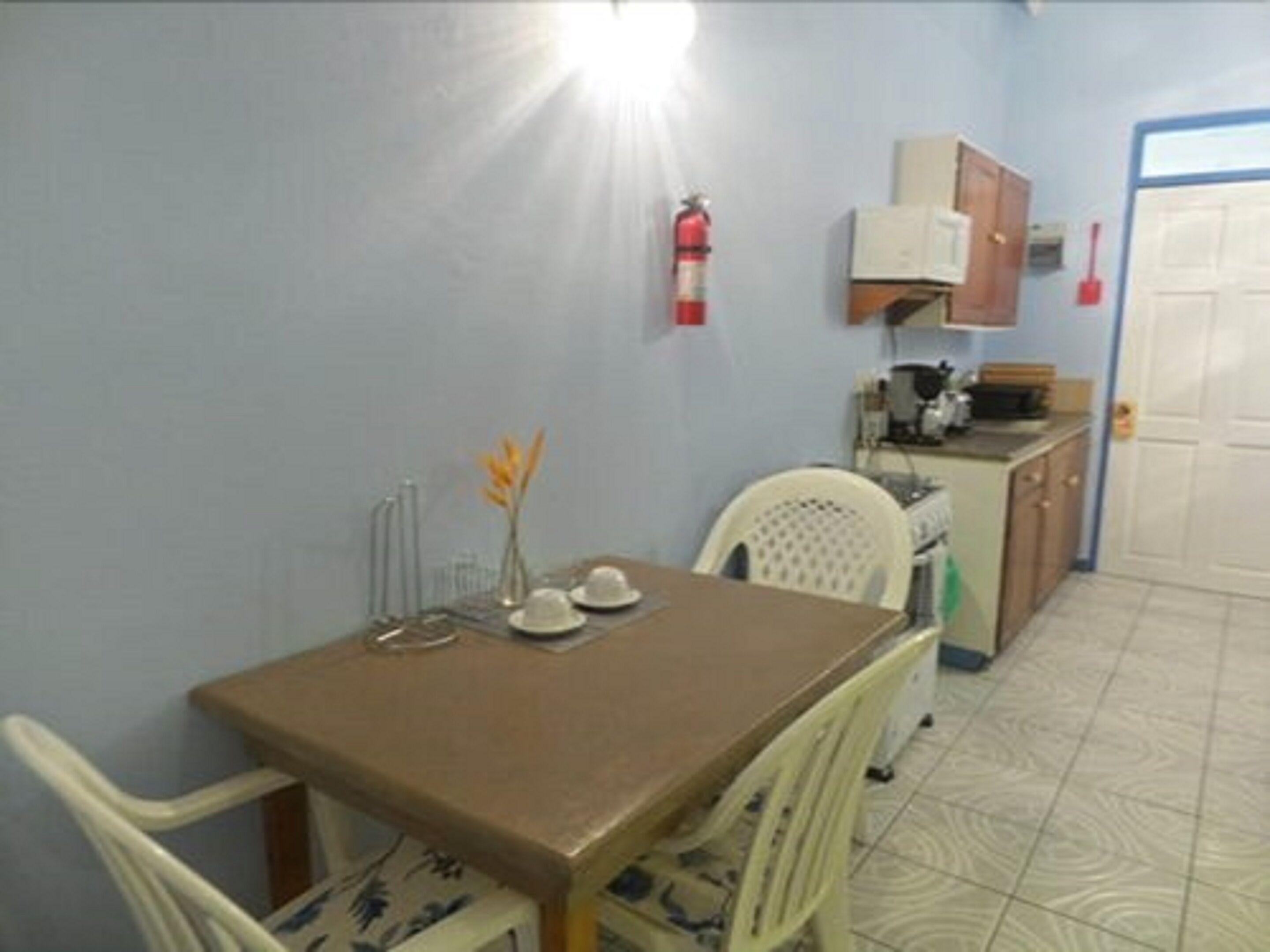 A small dining area with a table, chairs, a vase with flowers, and a kitchen area with cabinets and appliances.
