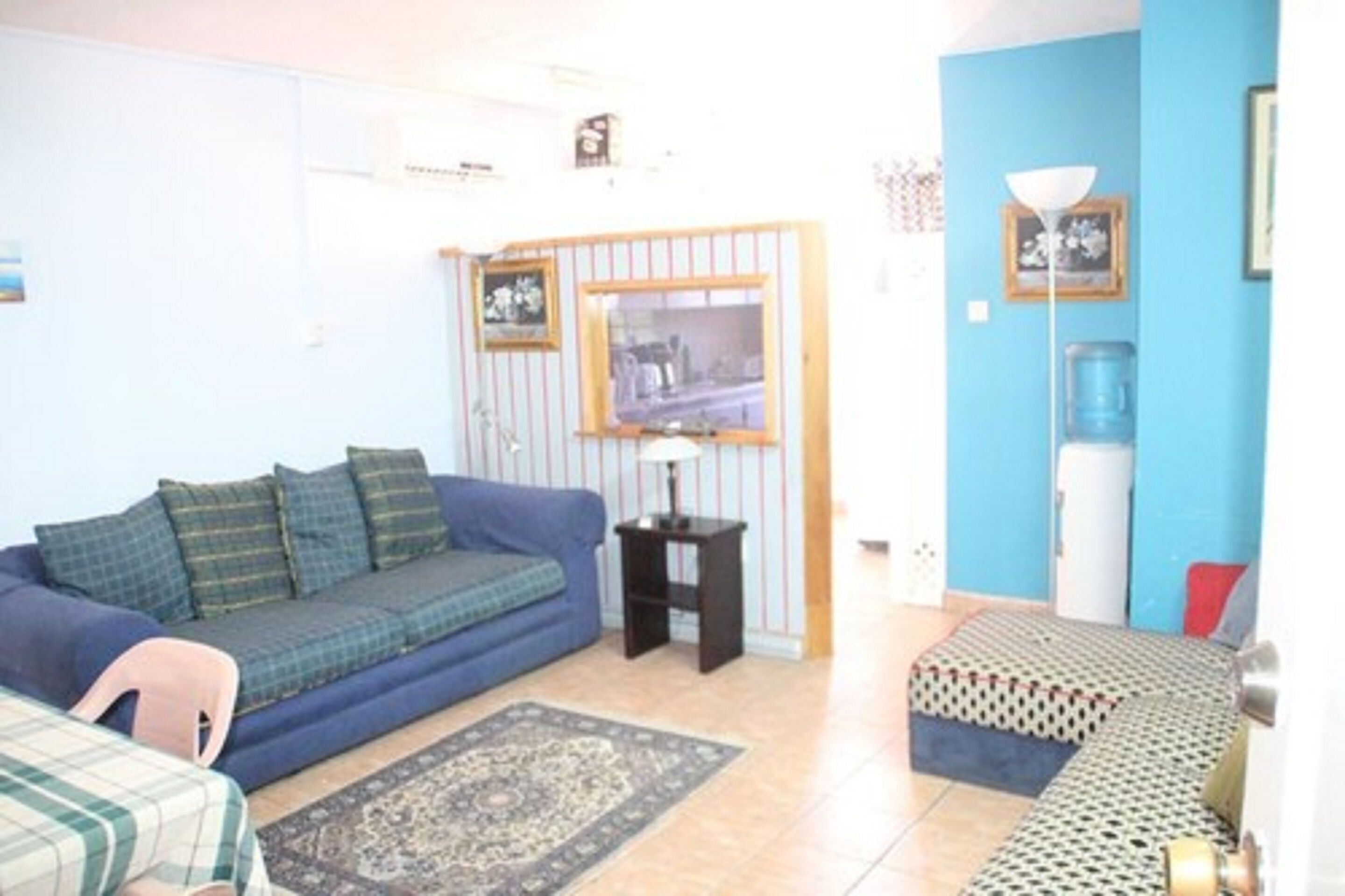 A living room with a blue sofa, a patterned rug, a small table, and a water dispenser.