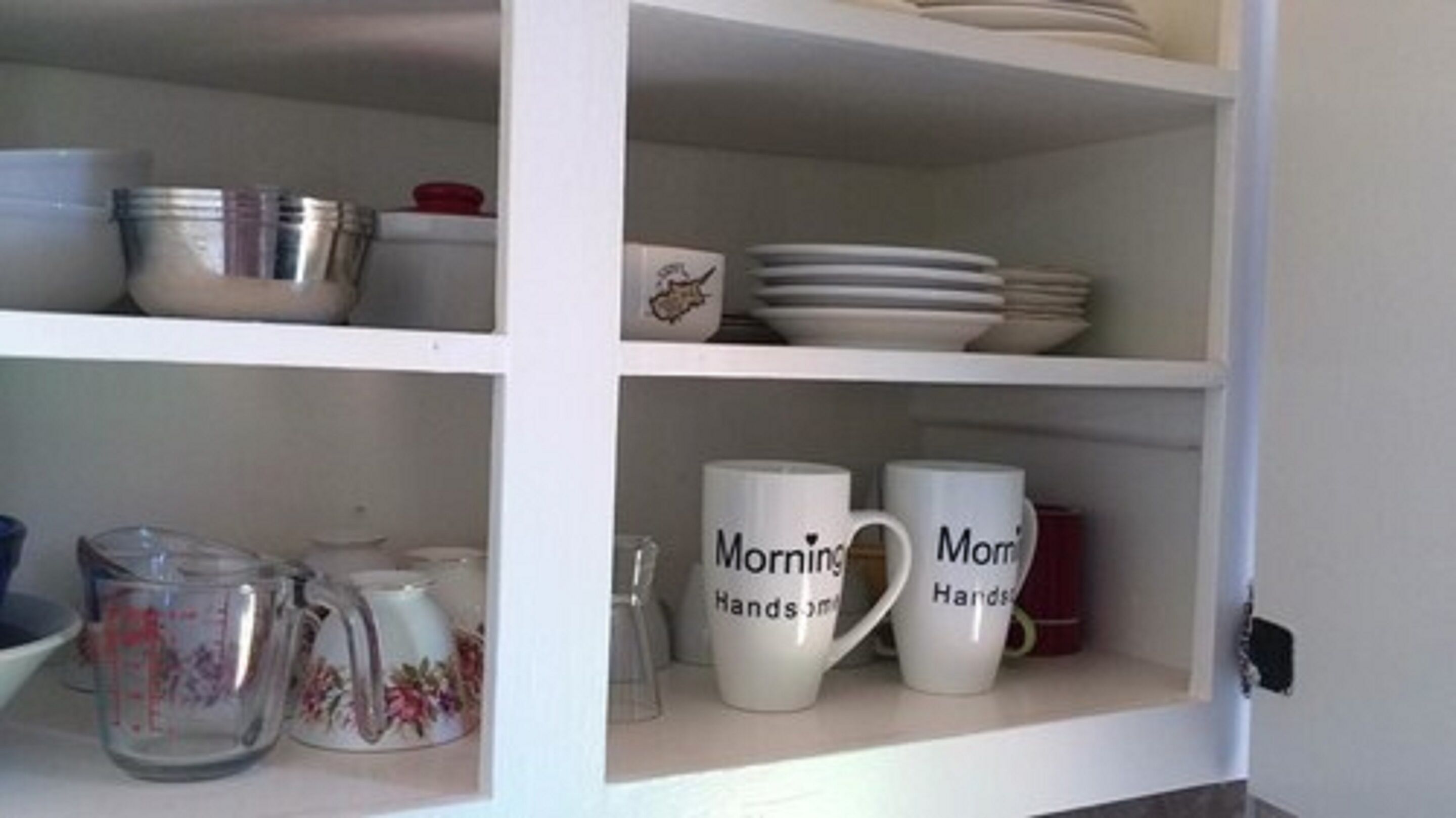 A kitchen shelf with various items including plates, a measuring cup, and two mugs with text.