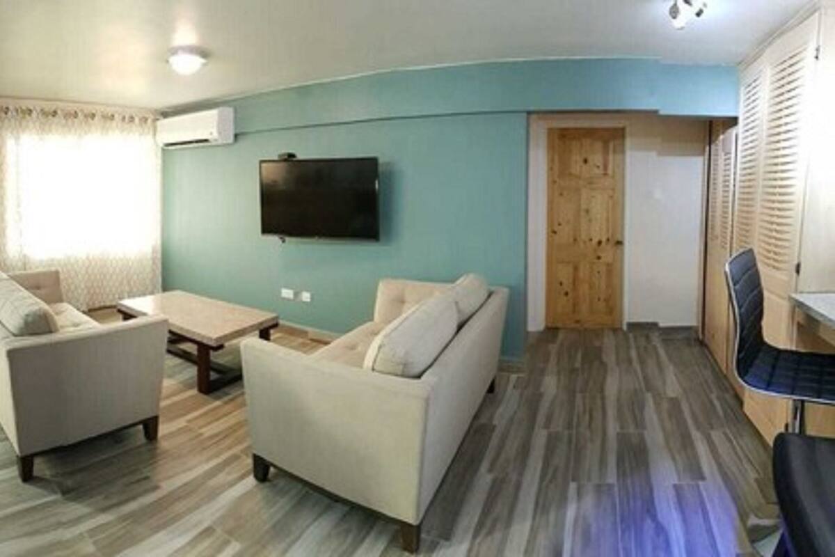 A living room with two sofas, a coffee table, a TV mounted on the wall, and a wooden door.