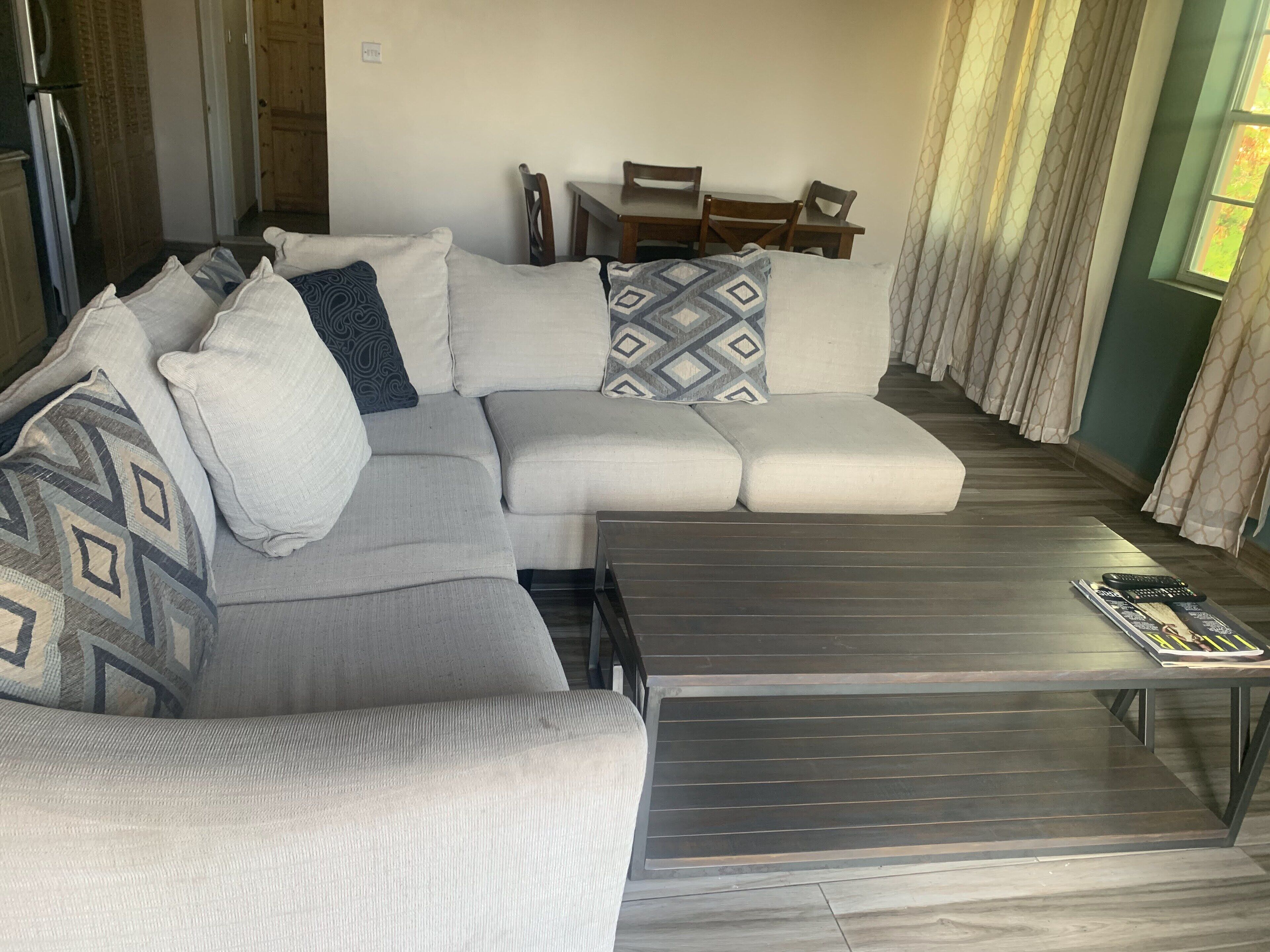 A modern living room with a grey sectional sofa, a wooden coffee table, and a dining area with a table and chairs.