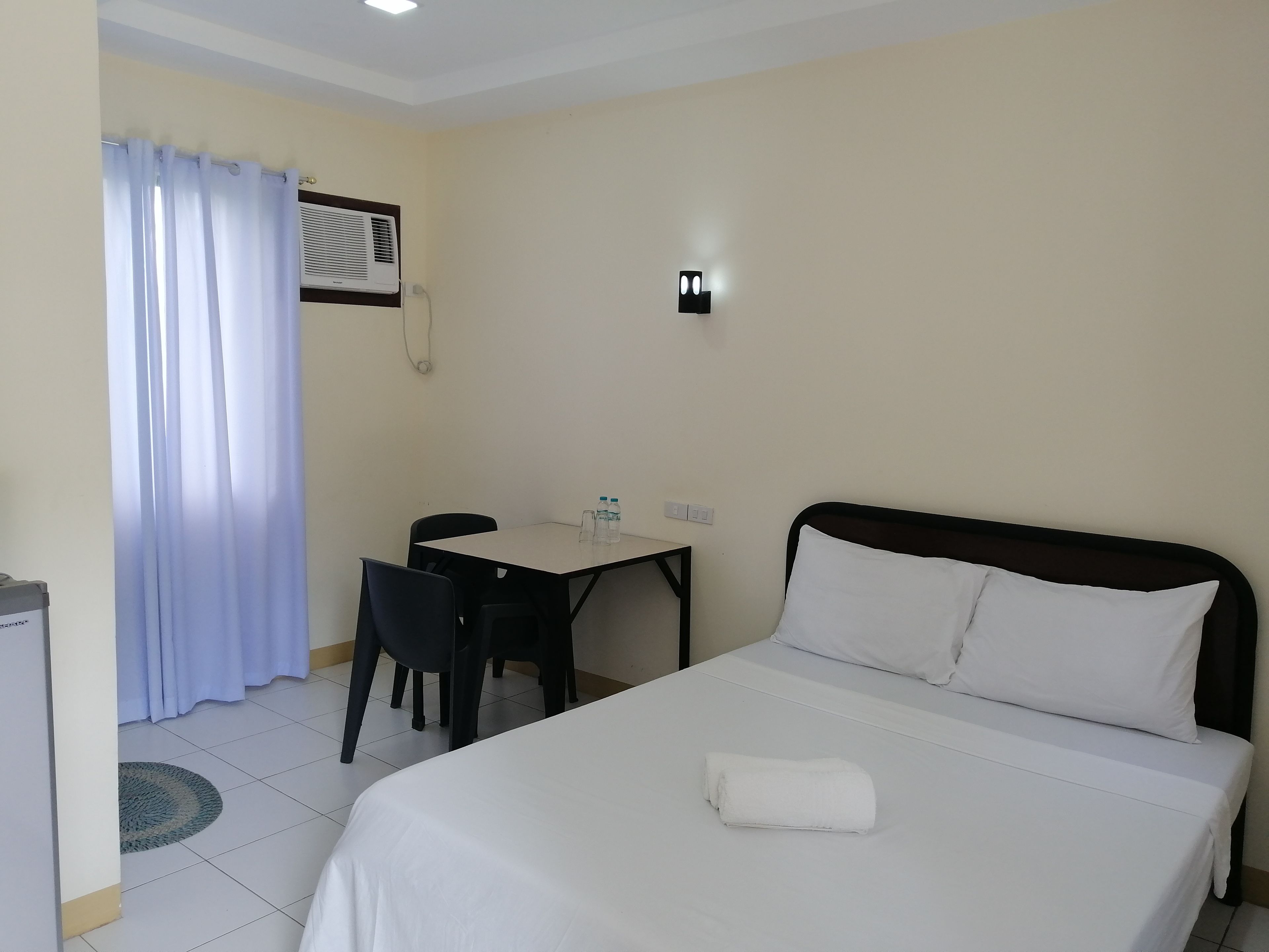 Habitación de hotel con cama, escritorio y silla. Hay una ventana con cortinas, un equipo de aire acondicionado y un teléfono en la pared.