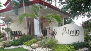A sign for 'Mira Diving Resort' surrounded by well-maintained landscaping, including a palm tree and various shrubs.