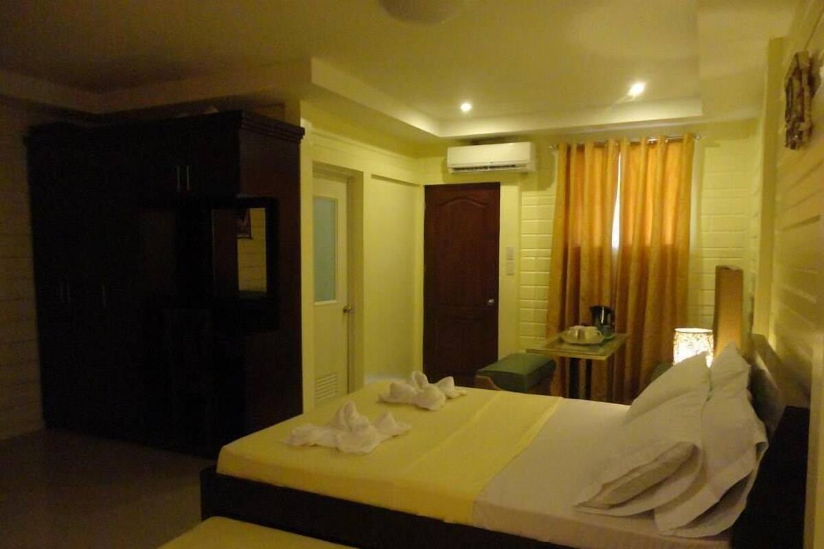 A hotel room with two beds, a desk, a chair, an air conditioning unit, and a curtain.