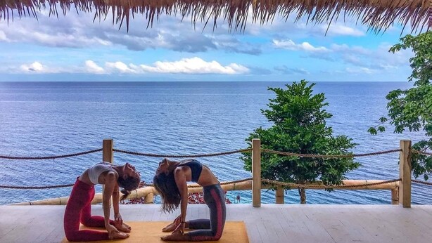 Two people practicing yoga on a mat with a view of the ocean.