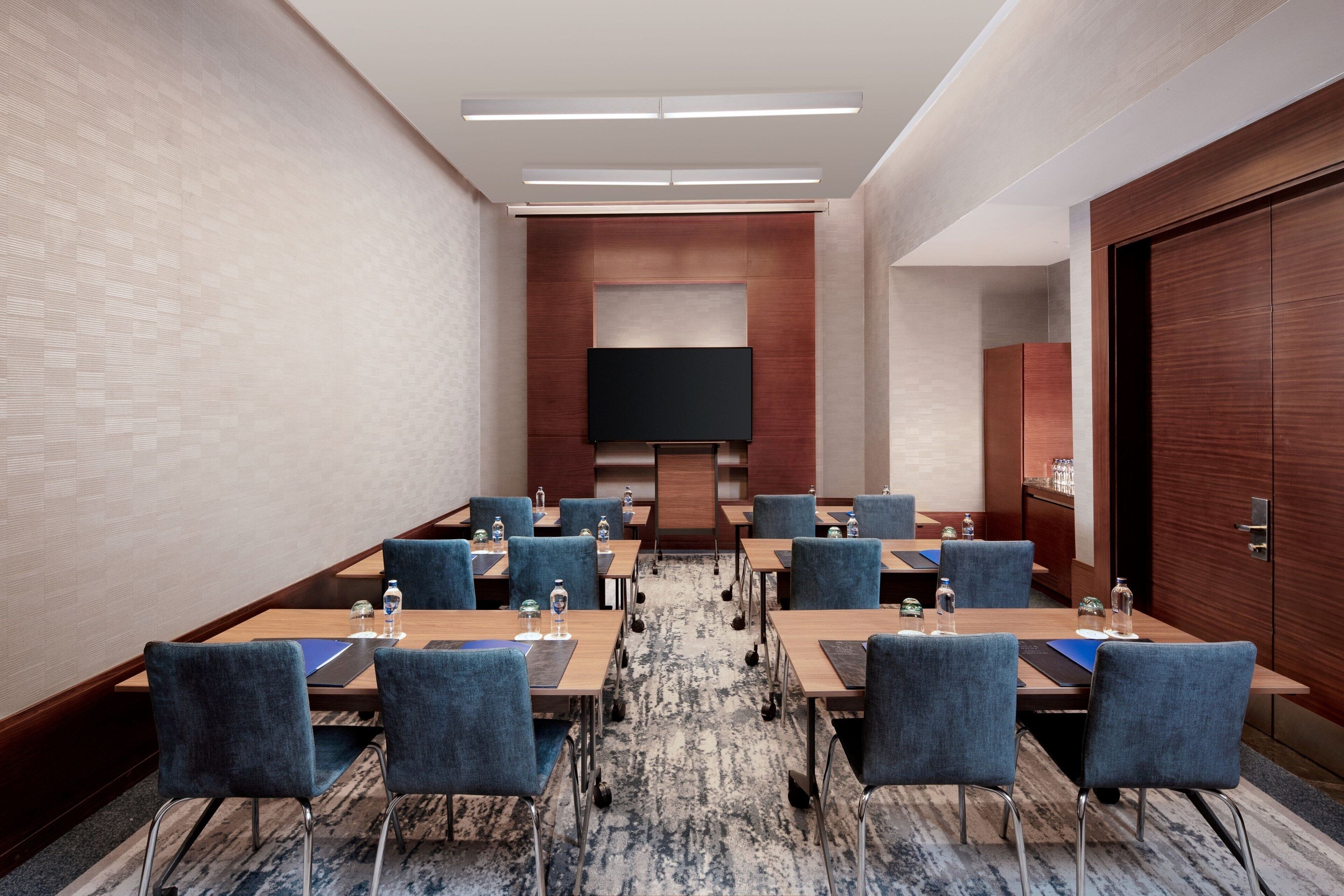 A conference room with multiple tables and chairs, a large flat-screen TV, and a wooden cabinet.
