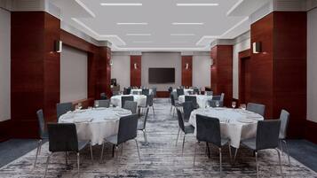 A conference room with round tables and chairs, a large screen, and a carpeted floor.