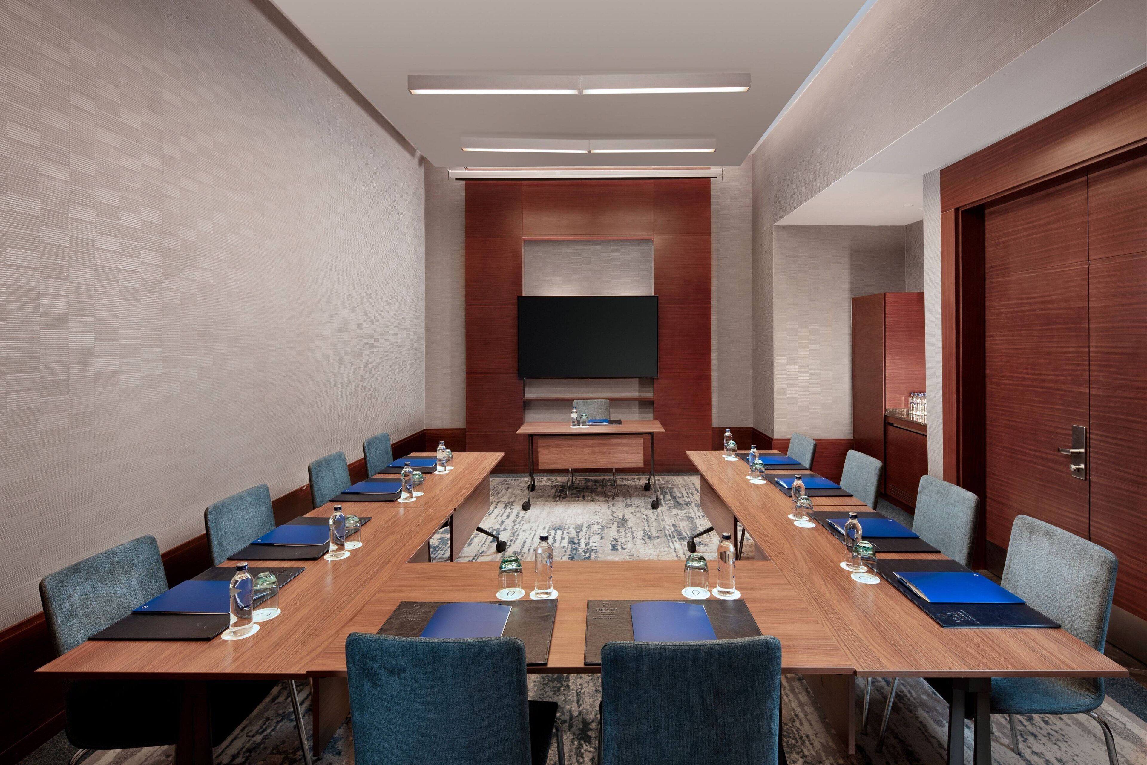 A conference room with a long table, chairs, water bottles, and a flat-screen TV.