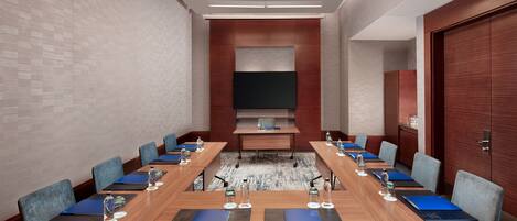 A conference room with a long table, chairs, water bottles, and a flat-screen TV.