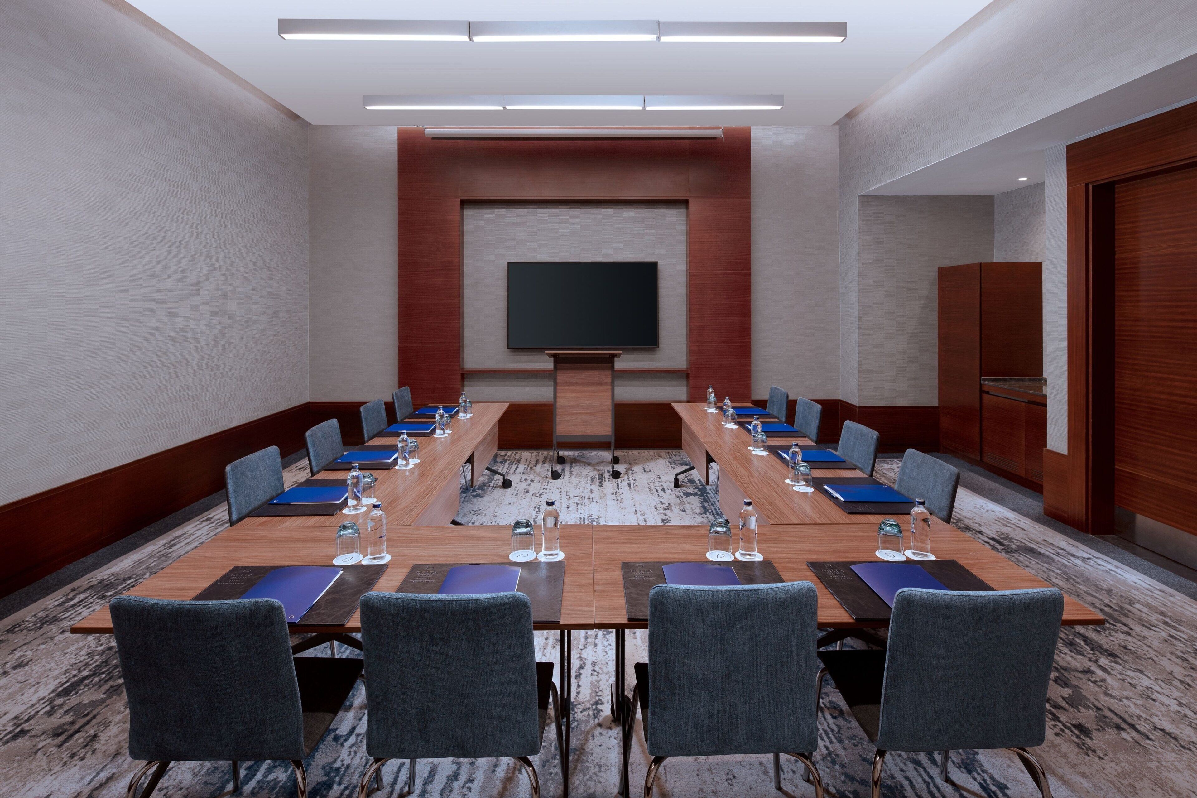Un salón de conferencias con una larga mesa, sillas, una pantalla y un atril.