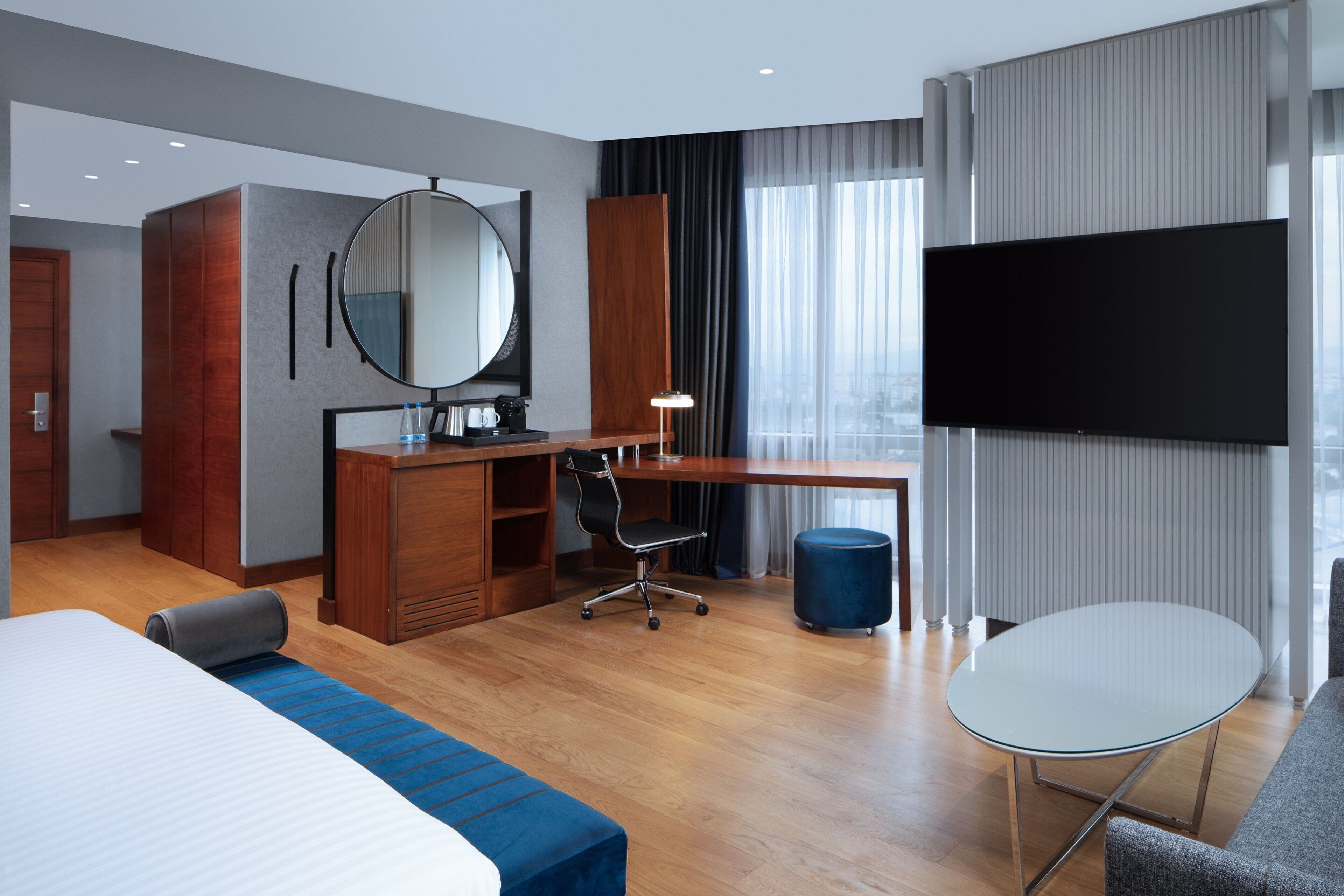 A modern hotel room with a bed, a desk, a chair, a TV, and a large window.