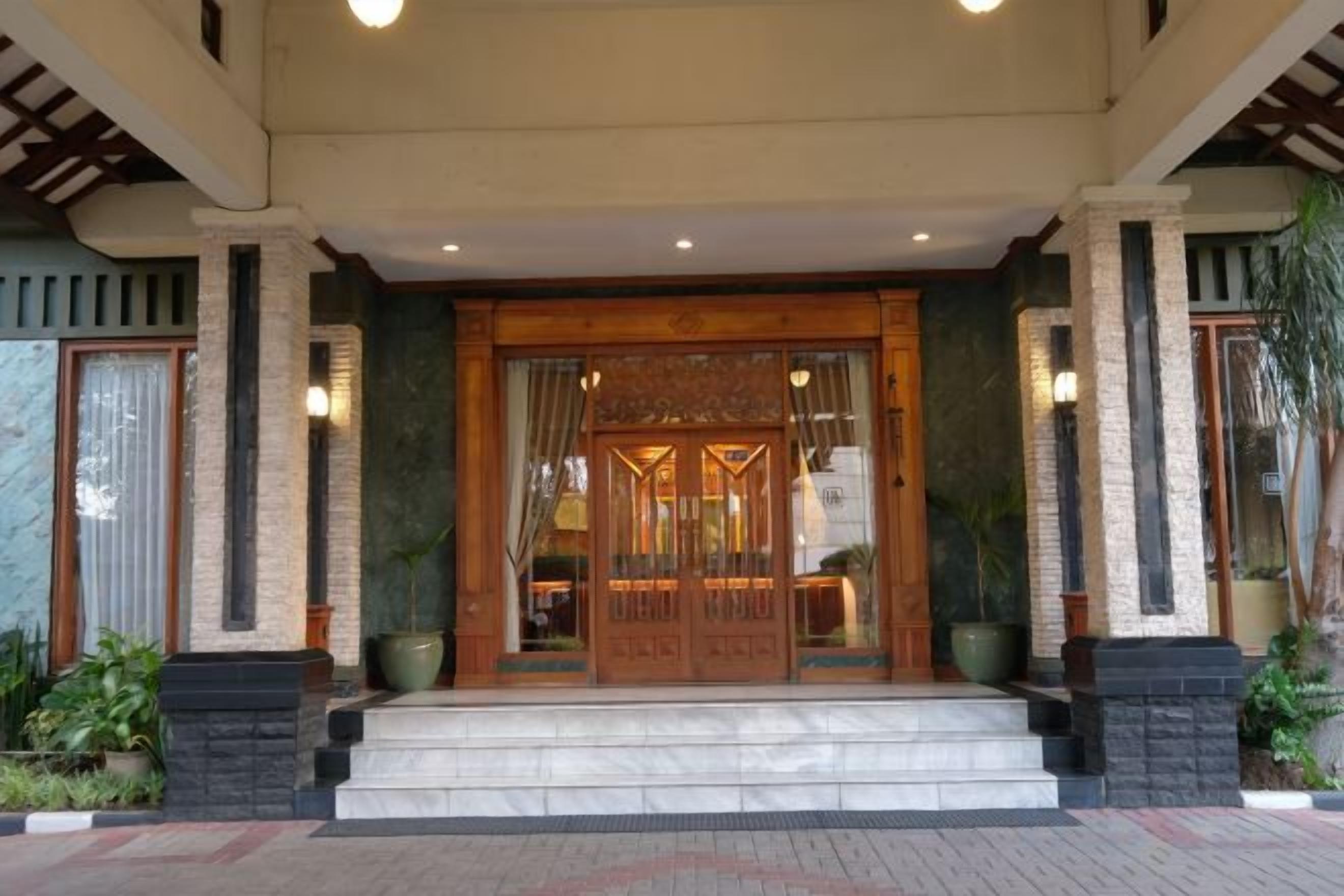 Entrada de hotel com porta de madeira, degraus e plantas em vasos.