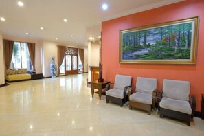 Eine Hotelhalle mit Rezeption, einer Sitzgelegenheit mit Stühlen und einem großen Gemälde an der Wand.