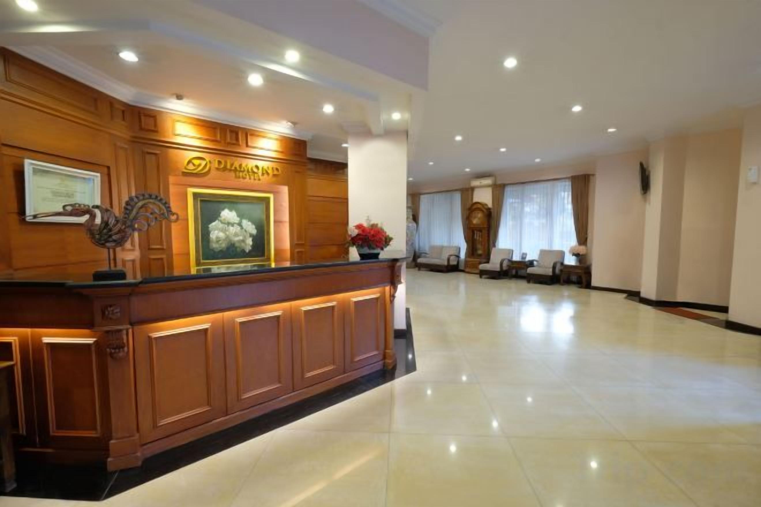 Uma área de recepção de hotel com balcão de madeira, quadros de certificados e uma grande janela com cortinas.