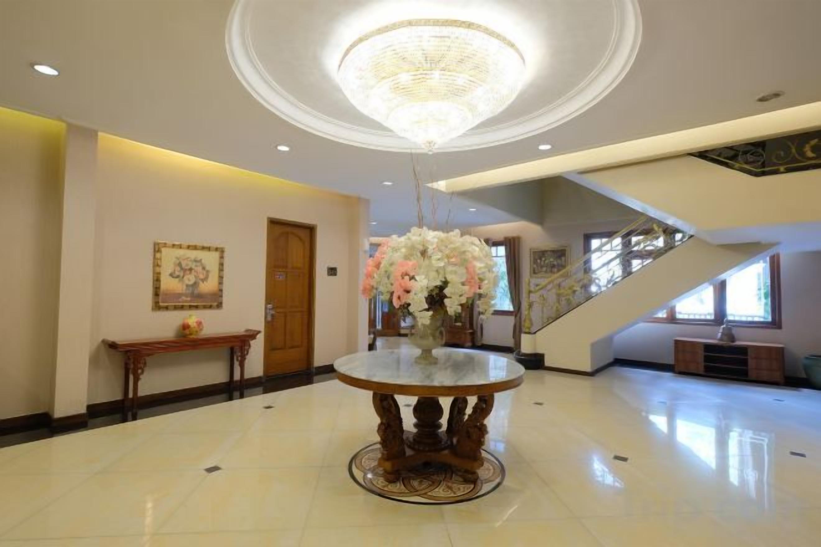A lobby with a round table, a chandelier, a staircase, and a door.