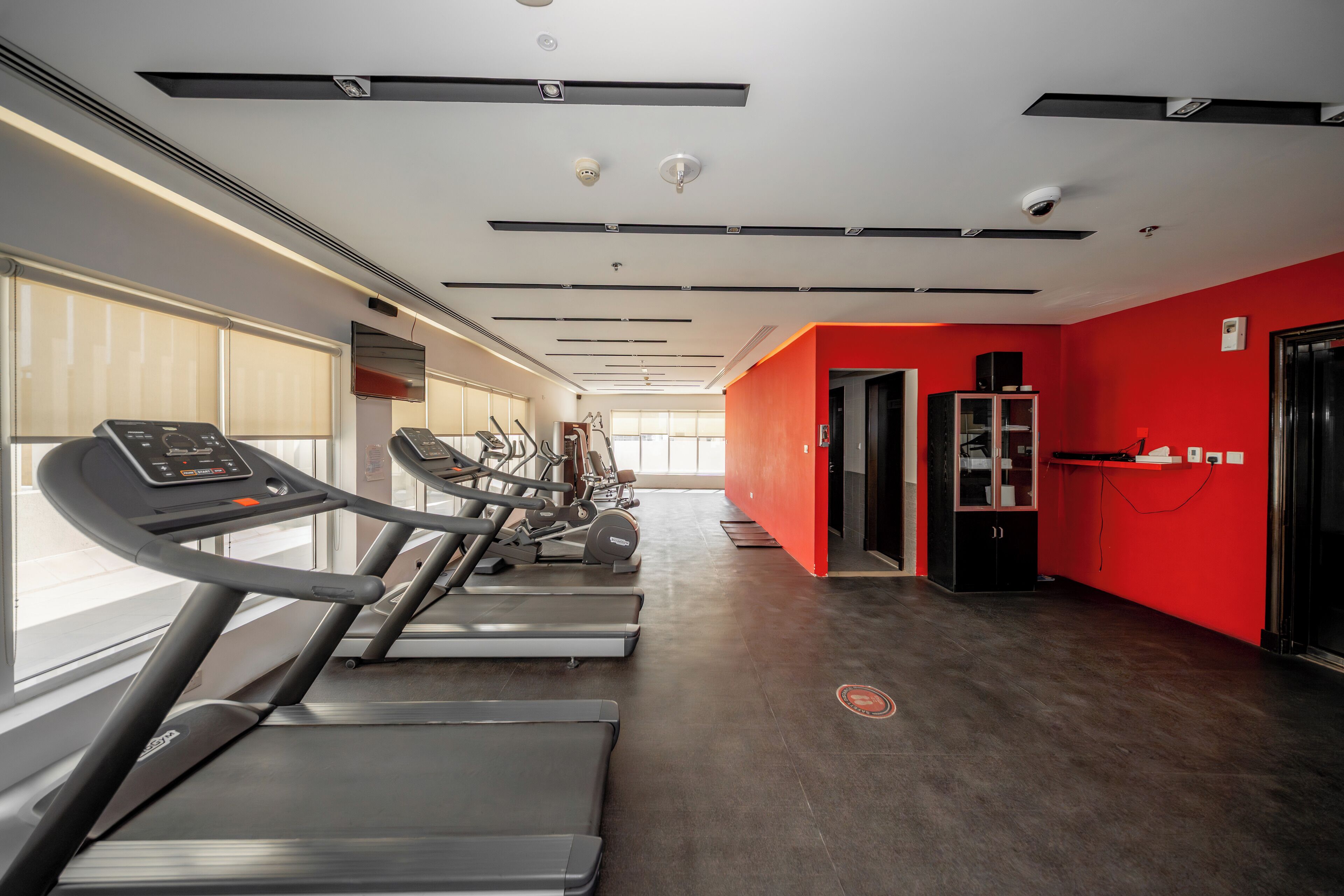 Ein Fitnessstudio mit Laufbändern, Trainingsgeräten und einer roten Wand als Gestaltungselement.