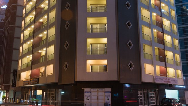 Ein mehrstöckiges Hotel mit beleuchteten Fenstern und Balkonen, einem Eingangsbereich auf Straßenniveau und einem modernen architektonischen Design.