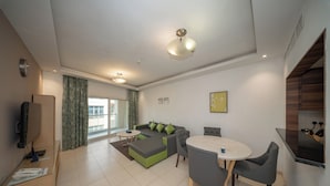 Ein modernes Wohnzimmer mit einer Couch, einem Esstisch und Stühlen. Ein Fernseher steht auf einem Schrank, ein Fenster mit Vorhängen und eine Deckenleuchte sind ebenfalls vorhanden.