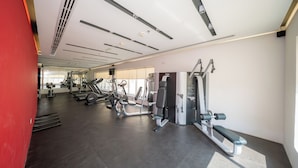 Ein modernes Fitnessstudio mit verschiedenen Trainingsgeräten, einer roten Wand und einem großen Fenster mit Tageslicht.