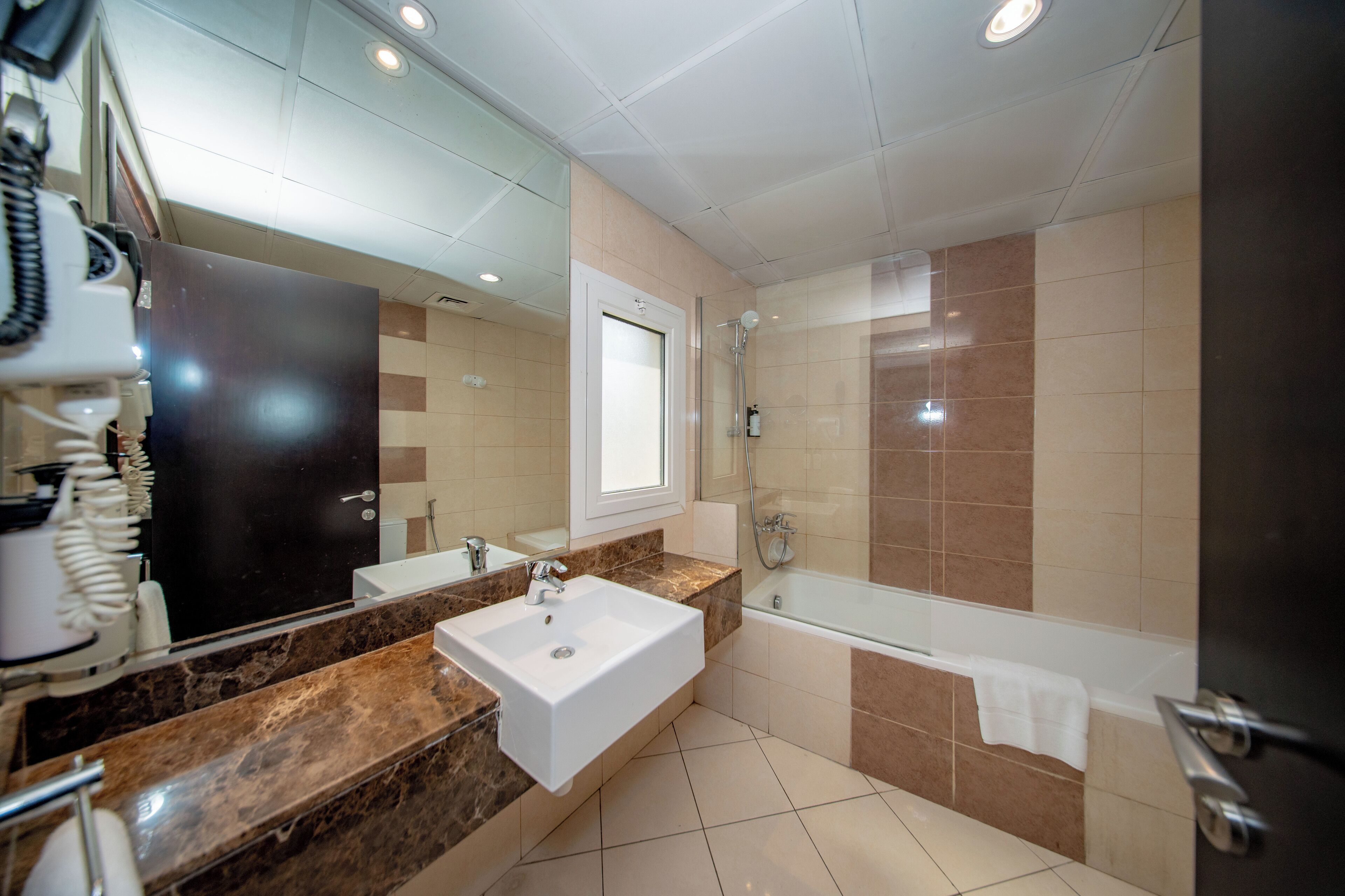 A modern bathroom with a large mirror, two sinks, a bathtub, and a shower.