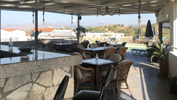 Eine Terrasse im Freien mit Steinboden, Korbmöbeln und hängenden Leuchten.