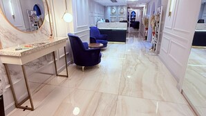 Un moderno vestíbulo de hotel con piso de mármol, una recepción y sillones azules, además de un espejo grande.