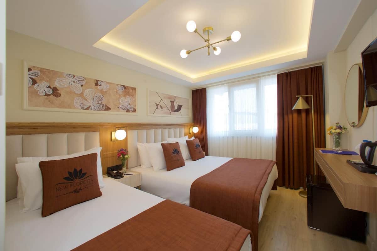 Habitación de hotel con dos camas, un escritorio, un televisor y obras de arte en las paredes.