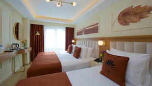 Habitación de hotel con dos camas, un escritorio, un espejo y un ventanal grande con cortinas.