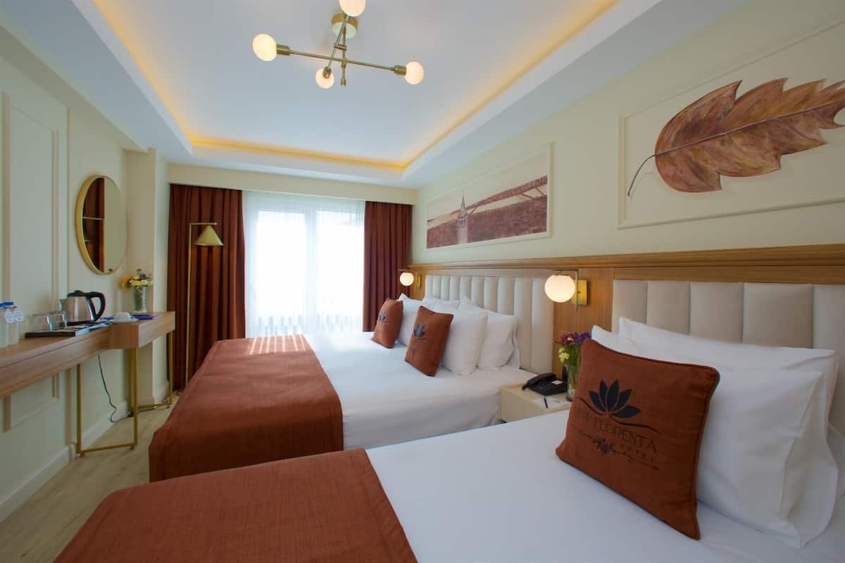 Habitación de hotel con dos camas, un escritorio, un espejo y un ventanal grande con cortinas.