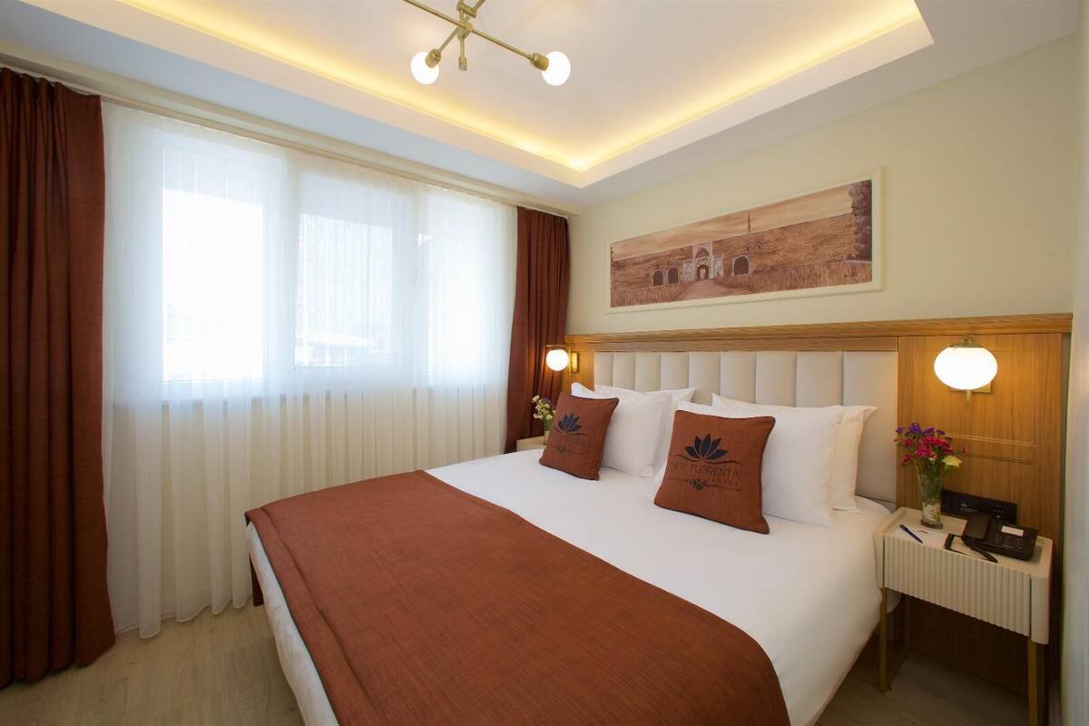 Habitación de hotel con una cama grande, una mesita de noche con lámpara y un cuadro en la pared.